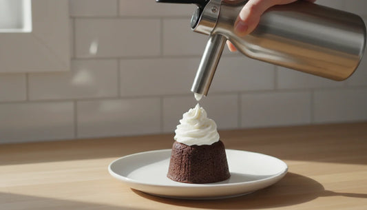 Stainless steel whipped cream dispenser dispensing fresh whipped cream onto a plated dessert on a kitchen counter